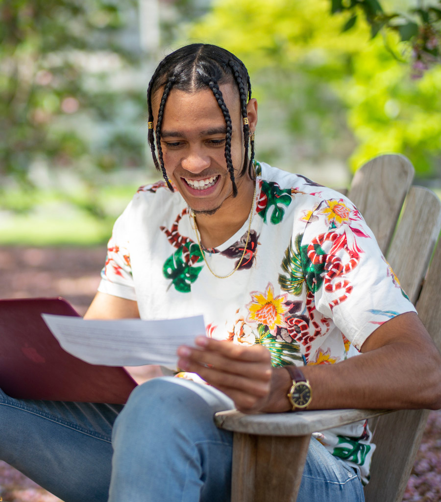 student smiling while working on his laptop and looking at a piece of paper