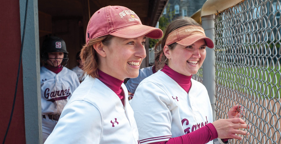 two Swarthmore softball players watching their team from the dugout