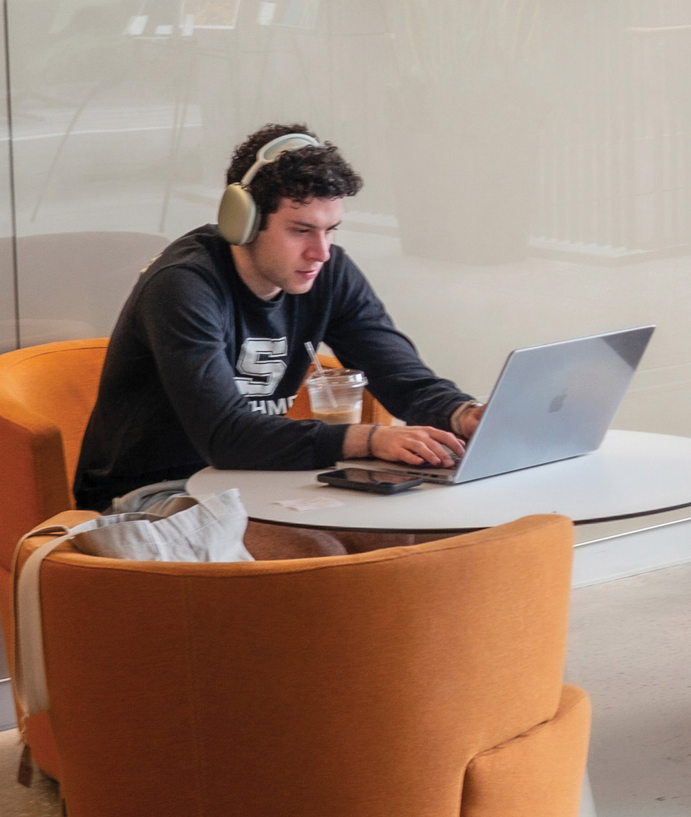 student sitting at a table with his headphones on while using his laptop