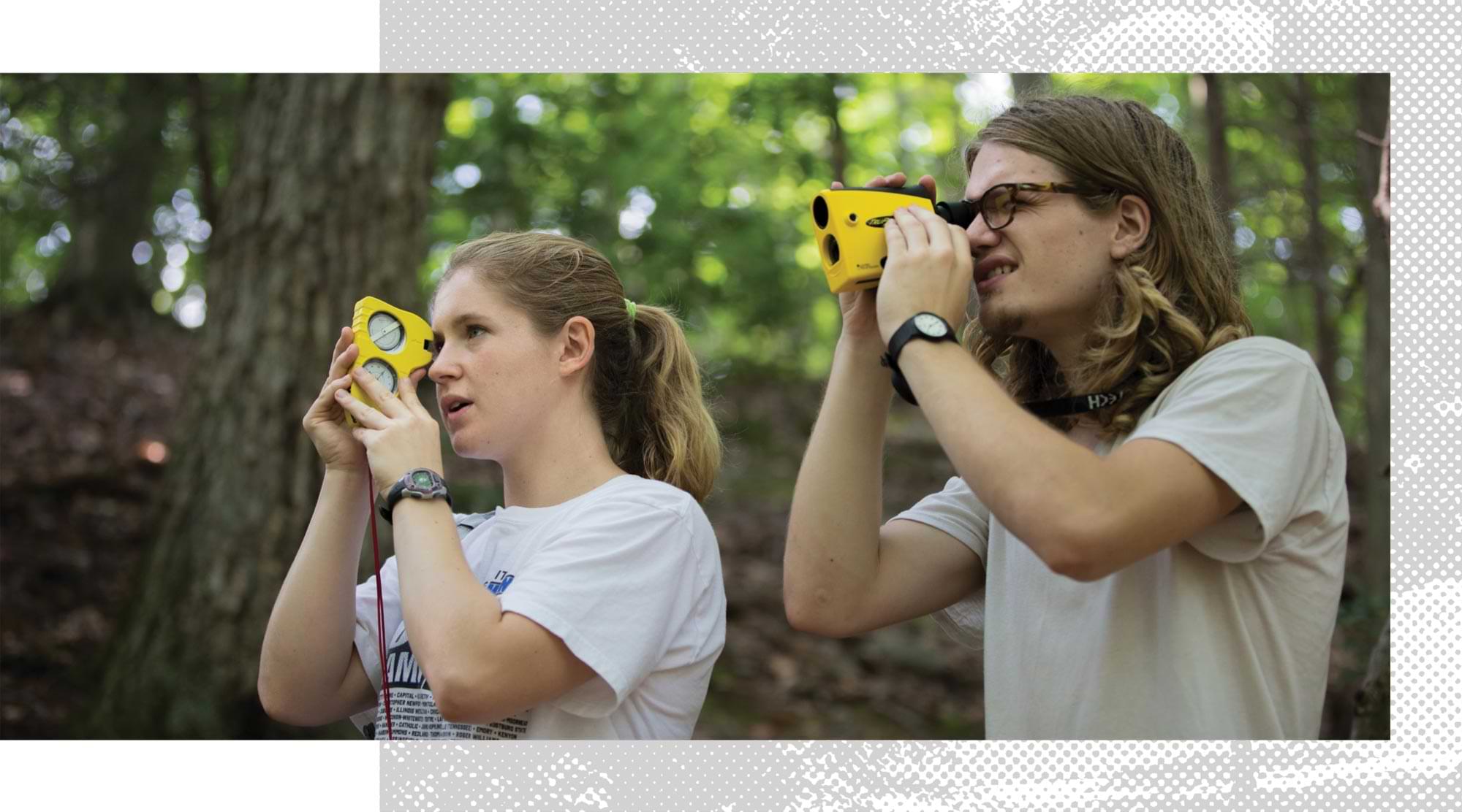two students use their binoculars to survey the landscape for their academic course