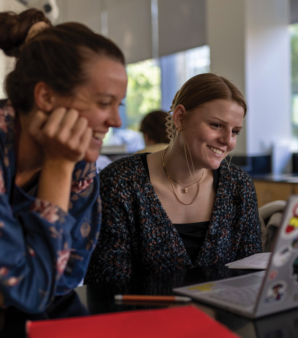 two students smiling while looking at a laptop