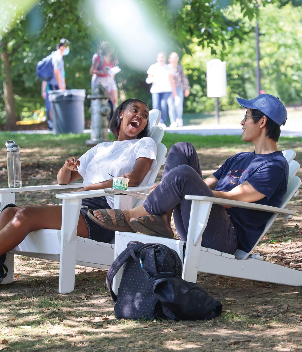 students sitting outdoors in white wooden lawn chairs