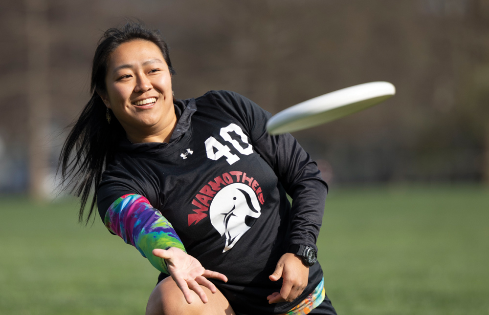 Person playing ultimate frisbee, throwing a white frisbee outdoors, wearing a black jersey with the number "40" and colorful sleeves.