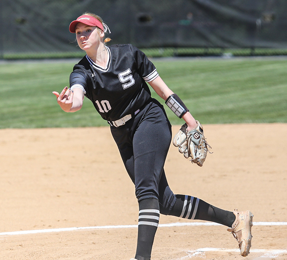 Softball player in black uniform pitching on a field.