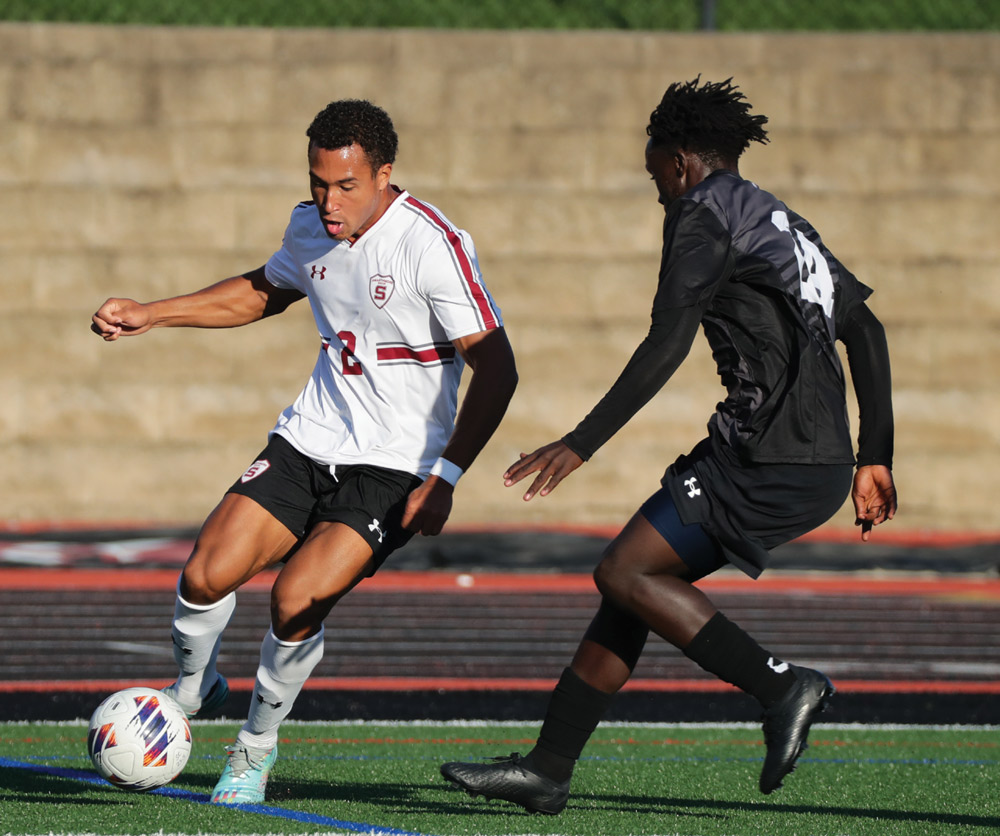 Two soccer players in action on a field, one wearing a white jersey and the other in black.