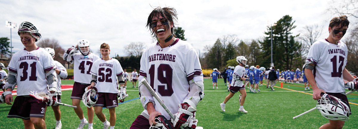 A group of lacrosse players in white and maroon uniforms on a turf field.