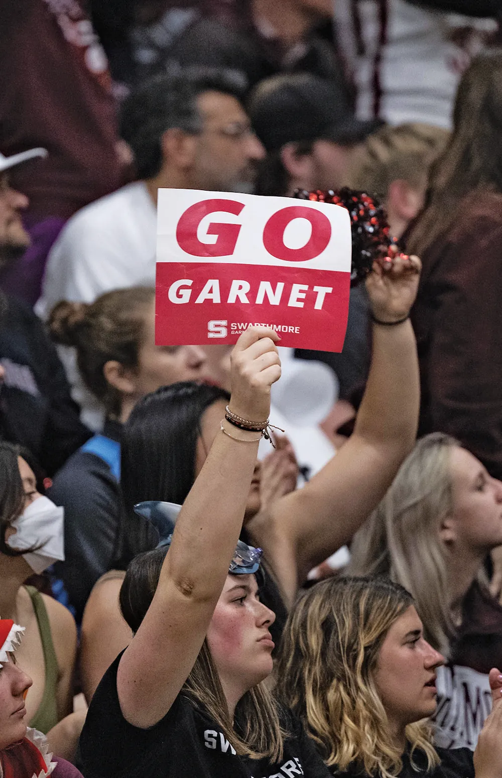 A person holds a red and white sign reading "GO GARNET" at a crowded event.