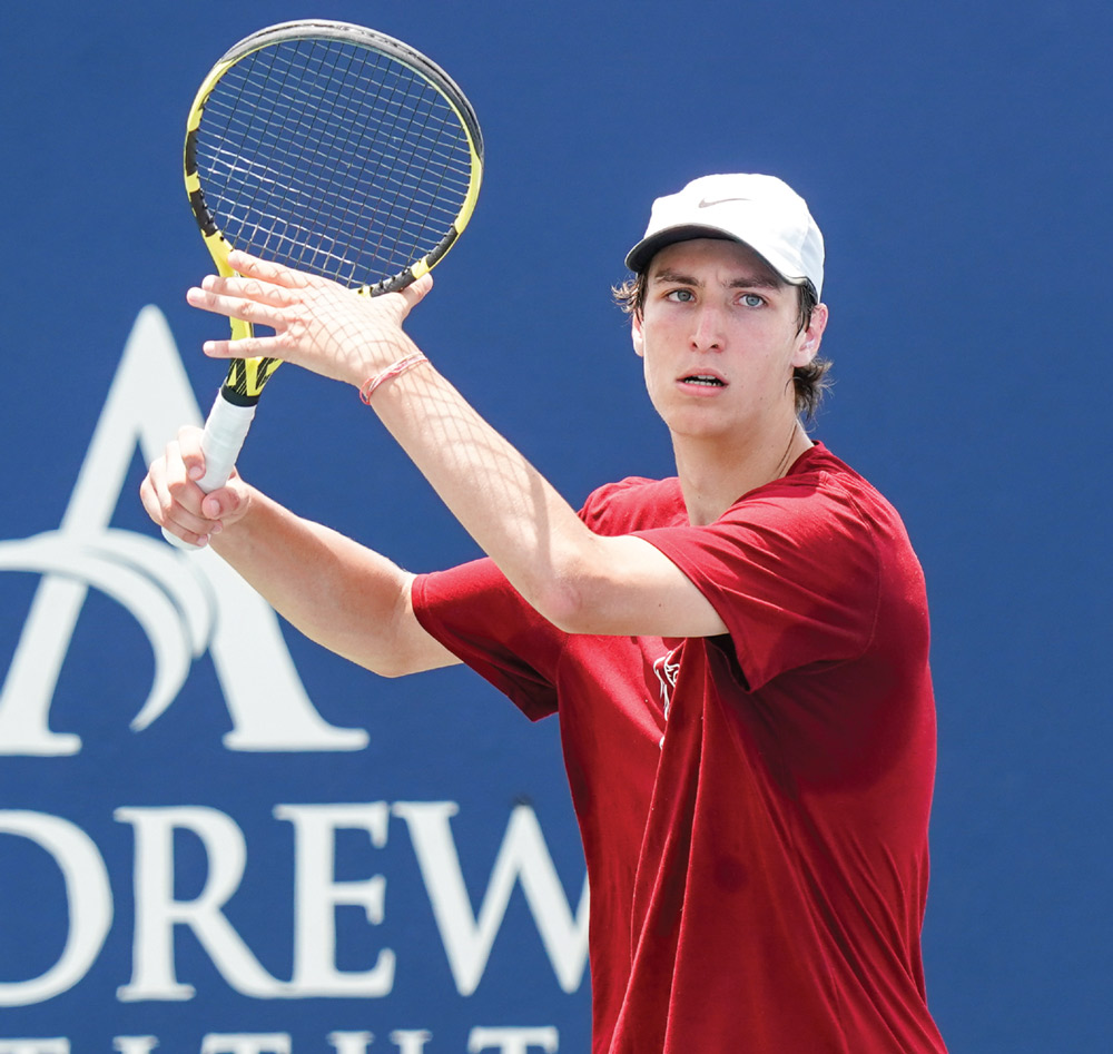 Tennis player in red shirt and white cap holding a racket.