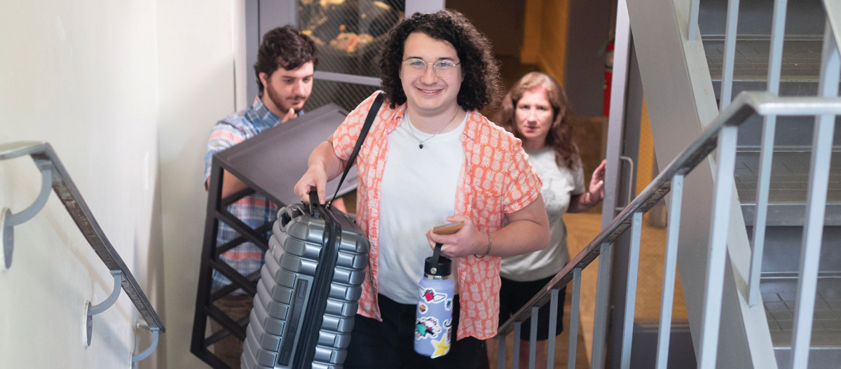 Three people carrying items up a staircase, with one person in the front smiling.