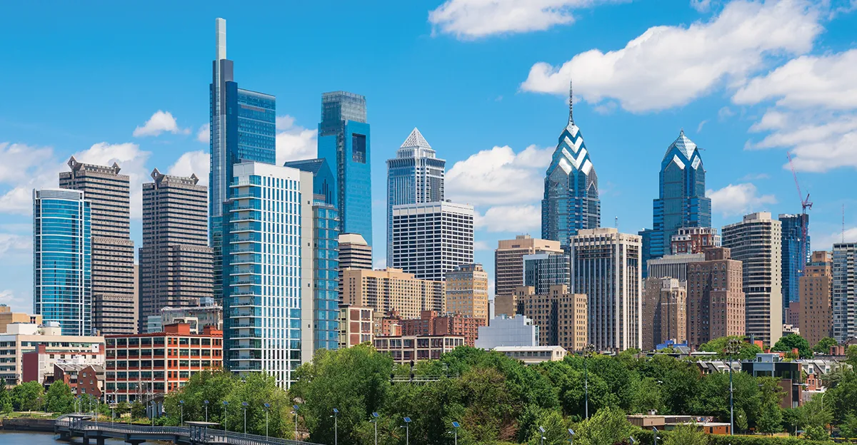 City skyline with tall buildings and a green foreground under a blue sky.