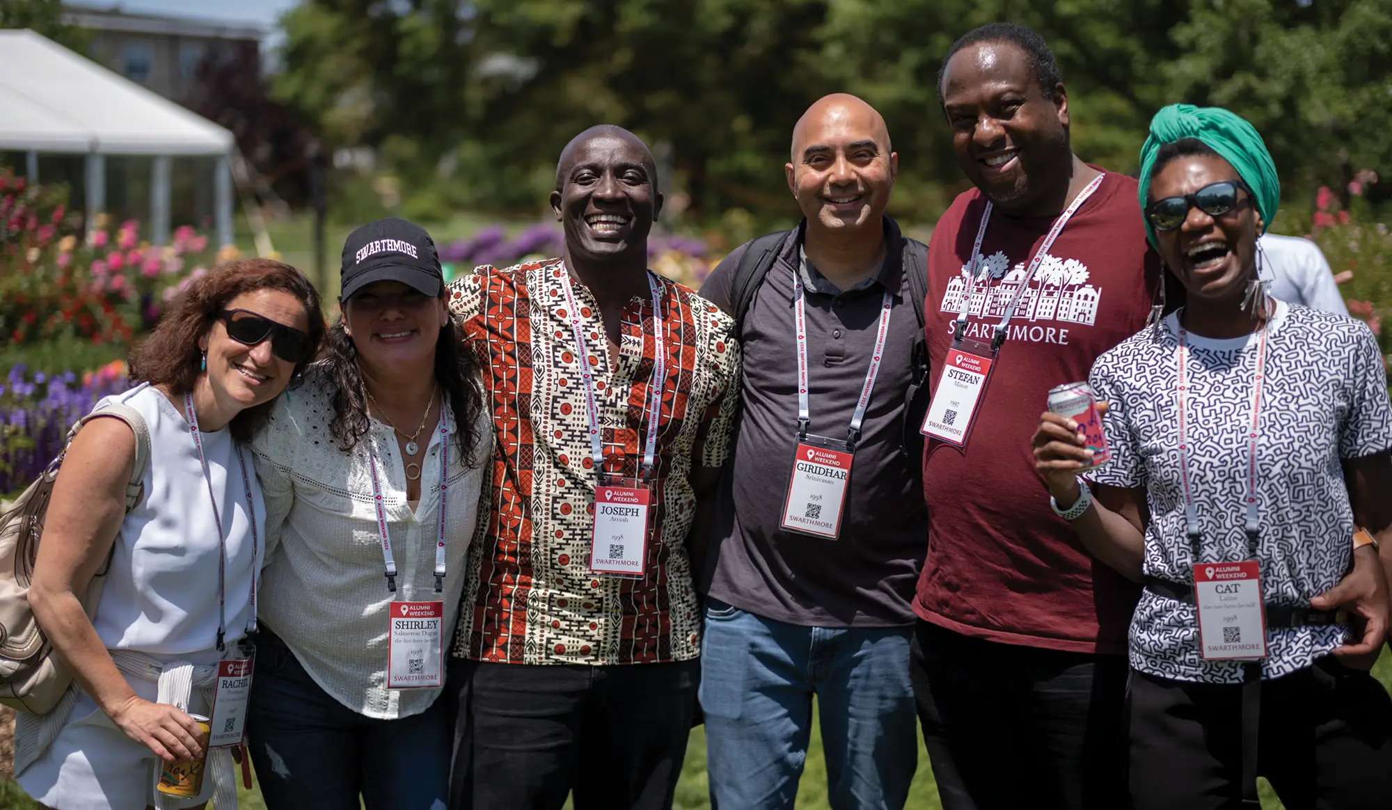 A group of smiling alumni wearing Swarthmore name lanyards pose together outdoors during an alumni weekend event.